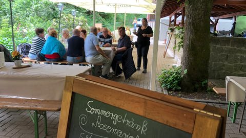Auf der Terasse der Waldgaststätte Bütthof sitzen Kunden unter Sonnenschirmen. Eine Bedienung bringt eine Tasse Kaffee (Foto: SWR, Christina Kist)