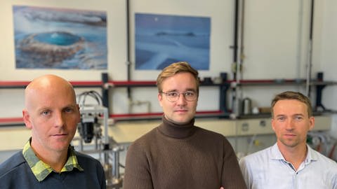 Foto von drei Männer in einer Reihe. Sie sind Forschende am Karlsruher Institut für Technologie und stehen in einem Laber des KITs. (Foto: SWR)