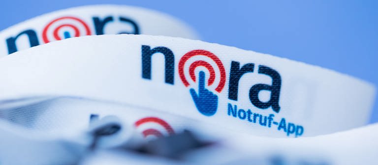 Das Logo der Notruf-App Nora ist auf ein Band gedruckt. (Foto: dpa Bildfunk, picture alliance/dpa | Rolf Vennenbernd)