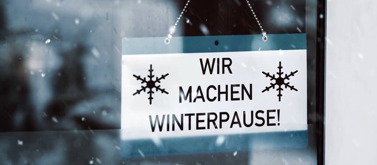 In einer Fensterscheibe hängt ein Schild mit der Aufschrift: "Wir machen Winterpause!" (Foto: IMAGO, Bihlmayerfotografie)