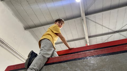 Ein Junge klettert in einer großen Halle mit Klettergerüsten, Matten und Seilen. (Foto: SWR)