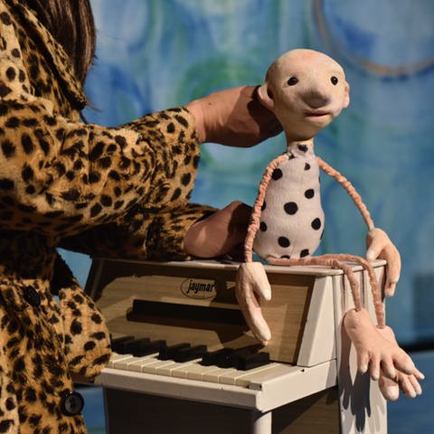 Eine stilisierte Puppe mit dünnen Ärmchen und Beinchen und einenm birnenförmigen Körper mit schwarzen Punkten, sitzt af einem Miniatur-Klavier. (Foto: Pressestelle, Theater Flunker-Produktionen)