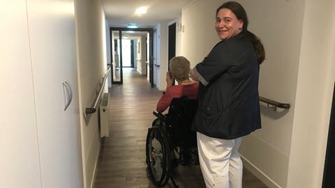 Sabrina Kaya von der AWO Karlsruhe schiebt ihre Patientin durch einen Flur. Sie arbeitet trotz der hohen Belastung gerne in der Pflege. (Foto: SWR)
