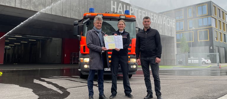 Oberbürgermeister Frank Mentrup steht mit zwei Feuerwehrleuten vor einem Feuerwehrauto für die Partnerstadt Winnyzja vor der Hauptfeuerwache in Karlsruhe. (Foto: SWR, Mirka Tiede)