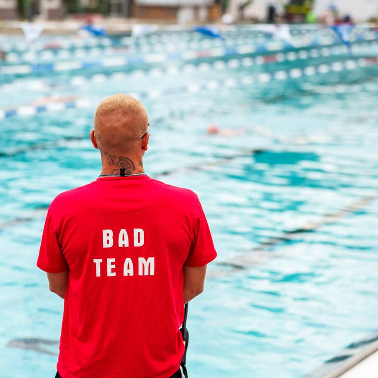 Symbolbild Sicherheitspersonal im Freibad. Mann im roten T-Shirt überwacht Schwimmbecken. (Foto: dpa Bildfunk, picture alliance/dpa | Andreas Arnold)