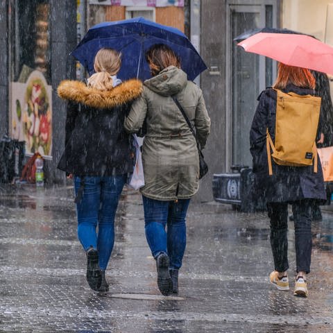 Der nasseste November in der Wettergeschichte: Drei Personen laufen mit Regenschirm durch den Regen (Foto: IMAGO, IMAGO / Michael Gstettenbauer)