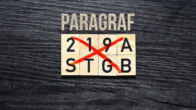 Über Bauklötzen steht das Wort "Paragraf". Auf denen Bauklötzen steht "219a STGB", was mit einem roten Keuz durchgestrichen wurde.