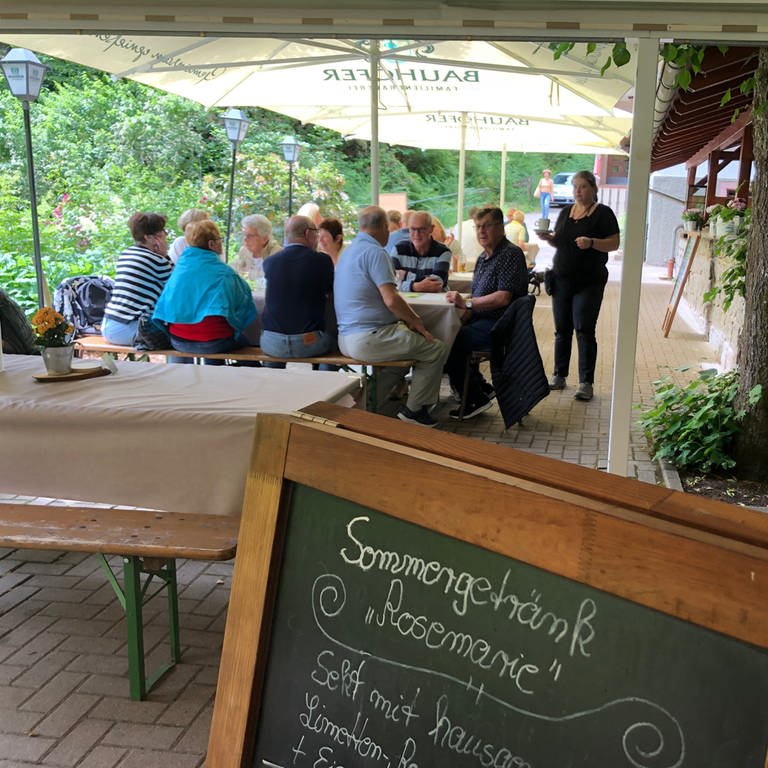 Auf der Terasse der Waldgaststätte Bütthof sitzen Kunden unter Sonnenschirmen. Eine Bedienung bringt eine Tasse Kaffee (Foto: SWR, Christina Kist)