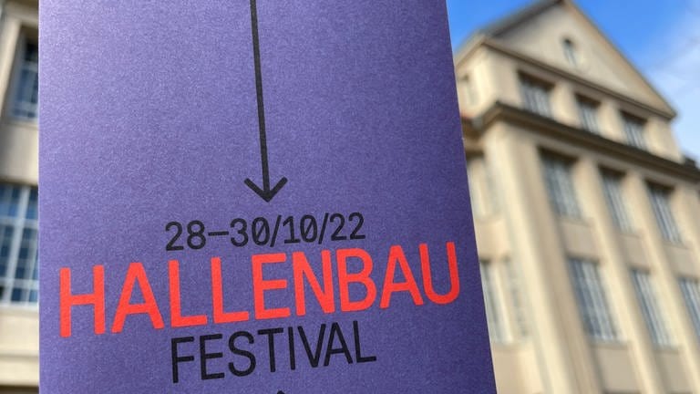 Im Voirdergrund Plakat mit der Aufschrift "Hallenbau-Festival 2022", im Hintergrund unscharf das ZKM-Gebäude. (Foto: SWR, Ines Kunze)
