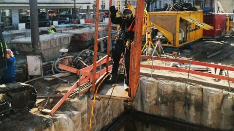 Ein Taucher wird in einem Arbeitskorb von einem Kran in die mit Wasser gefüllte Grube gelassen (Foto: Pressestelle, BAST (Badisches Staatstheater))