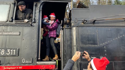 Mutter mit Kind auf dem Arm posiert auf der historischen Lok für einen Schnappschuss. Mutter und Kind tragen eine Nikolausmütze. (Foto: SWR, Teo Jägersberg)