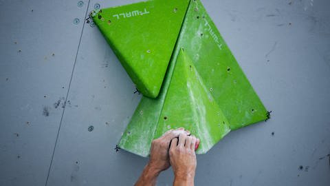 Hände greifen einen grünen Kunstoffgriff an einer Boulderwand  (Foto: picture-alliance / Reportdienste, Foto: Peter Kneffel )