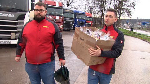 Medin Catic und Steffen Reiff von der Spedition mit einem Karton voller Geschenktüten für die Brummifahrer auf einem Autobahnrastplatz an der A8 bei Pforzheim. (Foto: SWR, Daniel Günter)