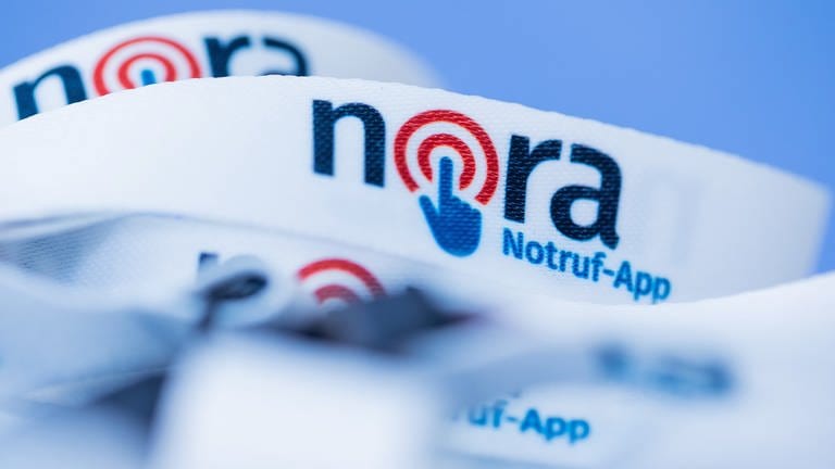 Das Logo der Notruf-App Nora ist auf ein Band gedruckt. (Foto: dpa Bildfunk, picture alliance/dpa | Rolf Vennenbernd)