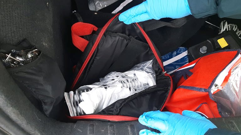 Eine Tasche in einem Kofferraum mit zahlreichen Tabletten. Zwei Hände mit blauen Handschuhen halten die Tasche auf. (Foto: picture-alliance / Reportdienste, dpa/Hauptzollamt Karlsruhe )