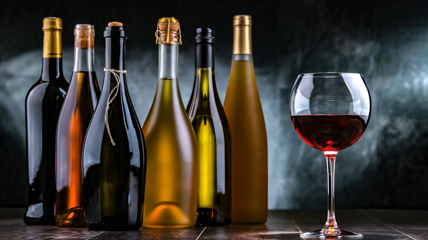 Ein Glas mit Rotwein und mehrere Flaschen (Foto: IMAGO, Zoonar)