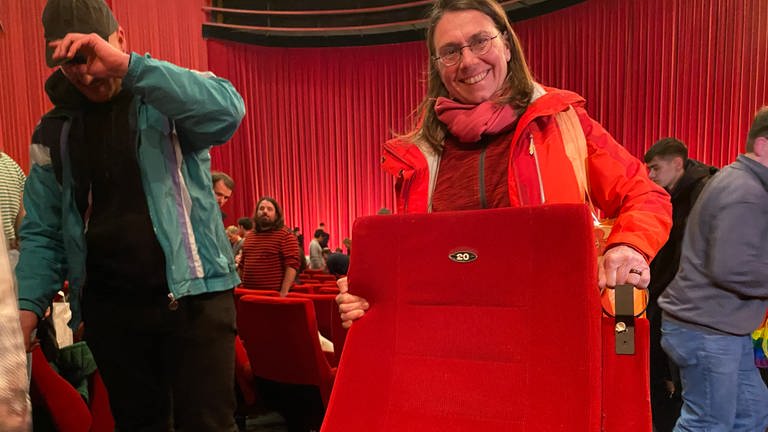 Eine Frau hält im Kino Schauburg in Karlsruhe stolz lächelnd einen roten Kinositz in den Händen. (Foto: SWR)