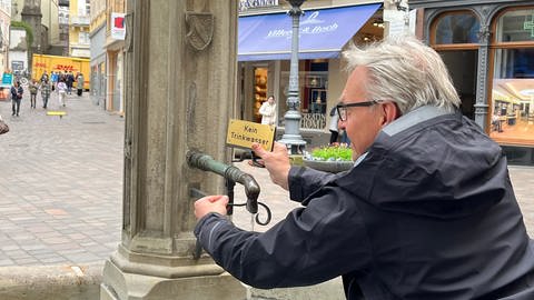 Kostenloses Trinkwasser kommt aus einem Brunnen in Baden-Baden. Bürgermeister Alexander Uhlig schraubt ein Schild "Kein Trinkwasser"ab (Foto: SWR, Sven Huck)
