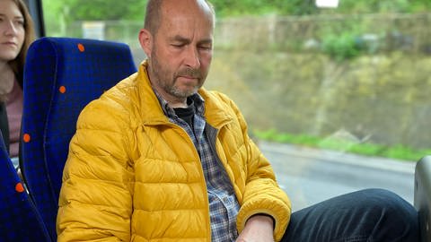 Ulrich Haug sitzt mit gelber Daunenjacke im Bus und liest (Foto: SWR, Markus Bender)