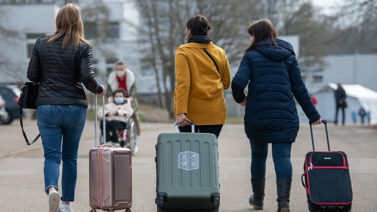 Drei Frauen, die wegen des Krieges nach Deutschland geflüchtet sind, ziehen ihre Koffer hinter sich her.
