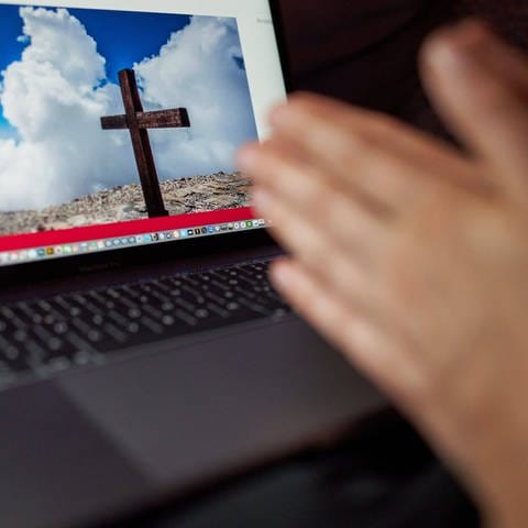 Symbolbild: Auf einem Computerbildschirm ist ein Kreuz zu sehen, davor Hände