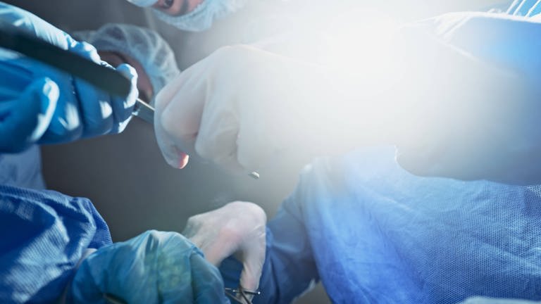 Symbolbild: Ärzte während einer Operation mit Skalpell in der Hand