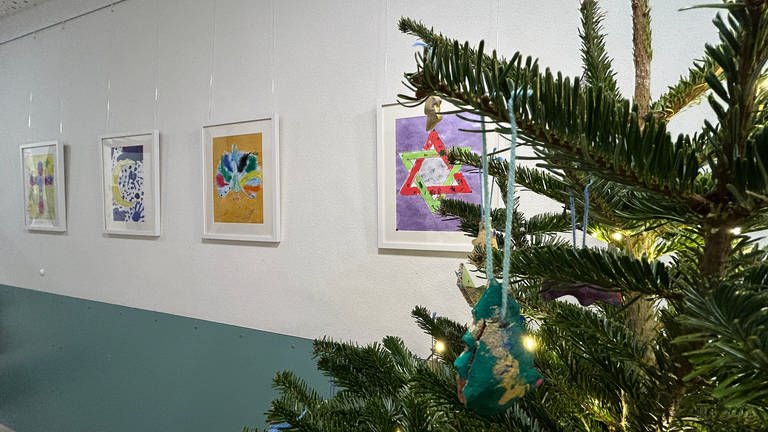 Im Gang in der Kita Irenicus in Pforzheim hängen neben dem Weihnachtsbaum Bilder von den Symbolen des Judentums, des Jesidentums, des Islams und des Christentums. 