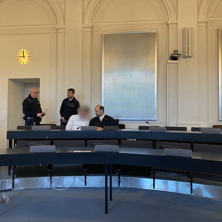 Der tatverdächtige Ehemann sitzt auf der Anklagebank am Landgericht Karlsruhe. Neben ihm sein Verteidiger und im Hintergrund sind zwei Justizbeamten zu sehen. Die Staatsanwaltschaft fordert eine lebenslange Gefängsnisstrage für den Angeklagten. Am Freitag soll das Urteil fallen. (Foto: SWR)