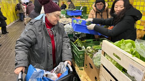 Eine ältere Frau wählt bei der Lebensmittelausgabe in der Unterführung am Kühlen Krug in Karlsruhe aus, was sie mitnehmen will.