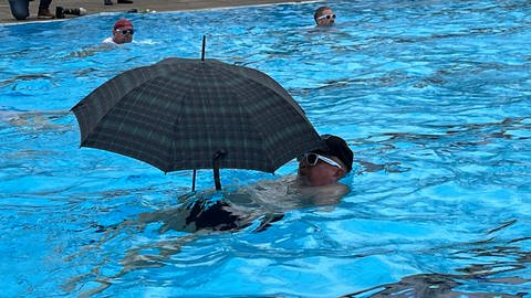 Ein Mann mit Schirm schwimmt im Wasser