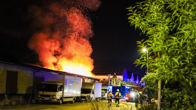 Hohe Flammen schlagen aus der Lagerhalle eines Möbelgeschäfts. Die Feuerwehr steht daneben und löscht den Brand im Kreis Karlsruhe.