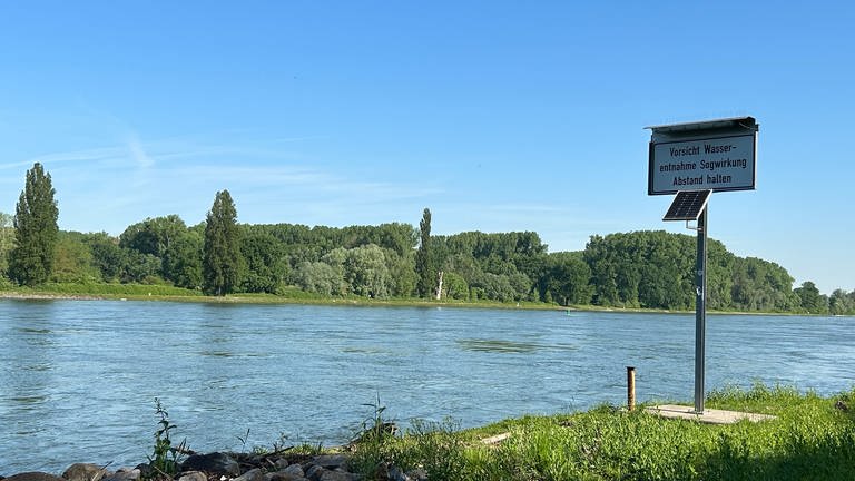 Blick über der Rhein bei Karlsruhe. Am Rand steht ein Schild, das vor Sogwirkung wegen Wasserentnahme warnt. 