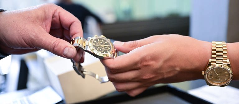 Eine Person übergibt der anderen eine Uhr. (Foto: dpa Bildfunk, picture alliance/dpa | Bernd Weißbrod)