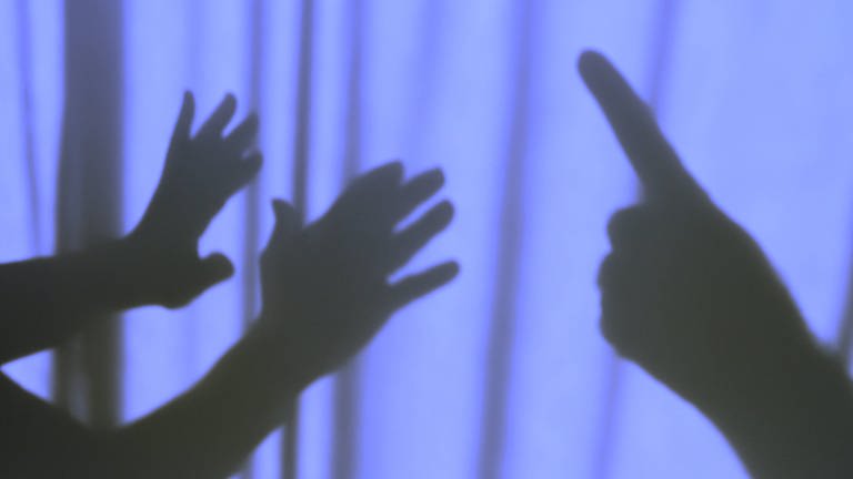 Zwei Hände im Schatten versuchen sich gegen drohende Hand zu wehren (Foto: IMAGO, Rolf Poss)