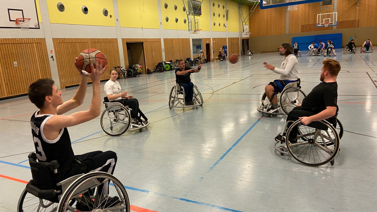 Fünf Personen im Rollstuhl werfen sich einen Basketball zu