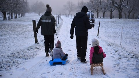 Ein Paar zieht zwei Schlitten mit Kindern auf einem verschneiten Feldweg. (Foto: PR-Video, René Priebe)