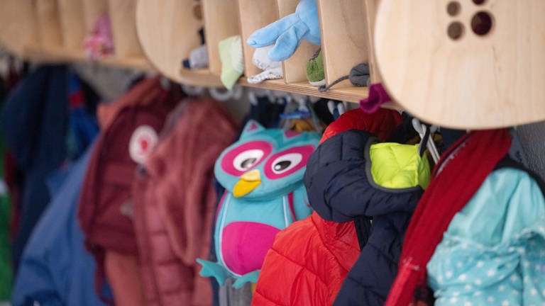 An einer Garderobe in einer Kita hängen Jacken und Kinderrucksäcke. (Foto: dpa Bildfunk, picture alliance/dpa | Marijan Murat)