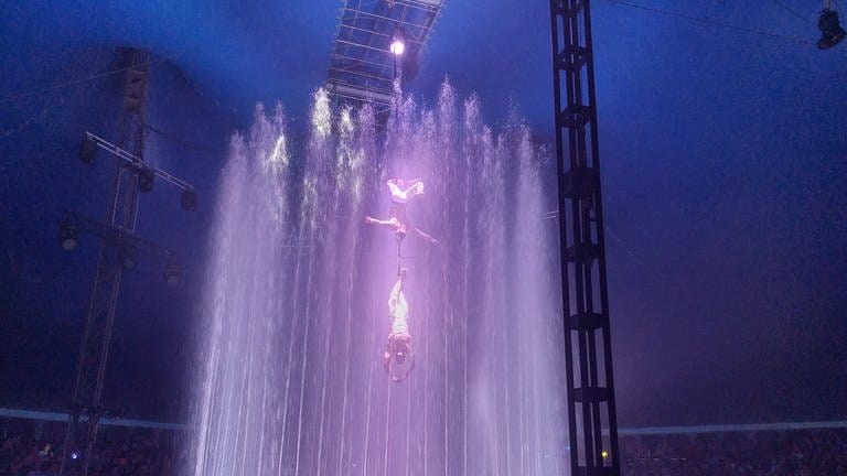 Zirkus Artisten schweben in der Luft umgeben von Wasserfontänen.  (Foto: SWR)