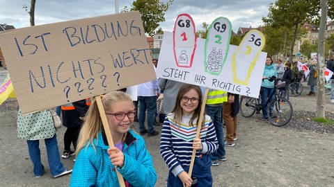Zwei Schülerinnen halten selbstgemachte Schilder in ihren Händen. Aufschrift: Ist euch Bildung nichts wert? Und: Steht ihr richtig? (Foto: SWR)