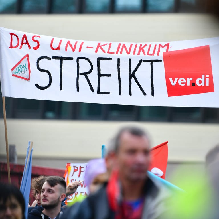 Streikende Beschäftigte halten bei einer Kundgebung vor dem Universitätsklinikum Heidelberg ein Transparent mit der Aufschrift «Das Uni-Klinikum streikt» in die Höhe (Foto: dpa Bildfunk, picture alliance/dpa | Uwe Anspach)