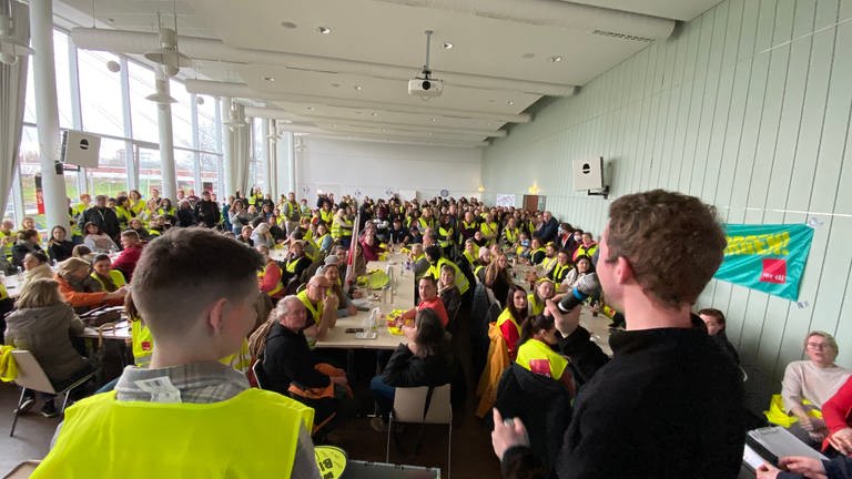 Streikende sitzen in gelben Westen an Tischen im Gewerkschaftshaus in Mannheim. (Foto: SWR)