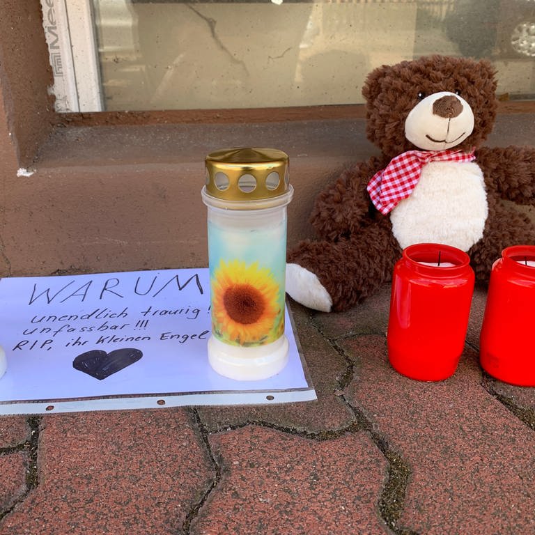Kerzen und Kuscheltiere auf Bürgersteig in Hockenheim und ein Baltt mit der Frage "warum?"