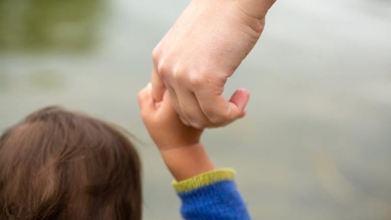 Eine erwachsene Person hält ein Kind an der Hand