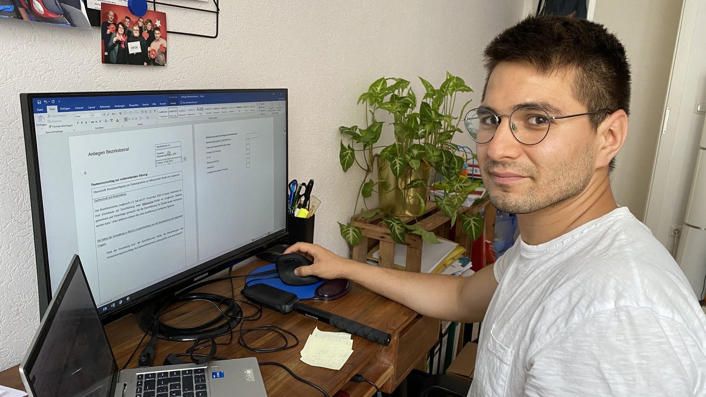 Karim Baghlani am Schreibtisch vor Computer mit Maus in der Hand und Pflanze im Hintergrund (Foto: SWR)