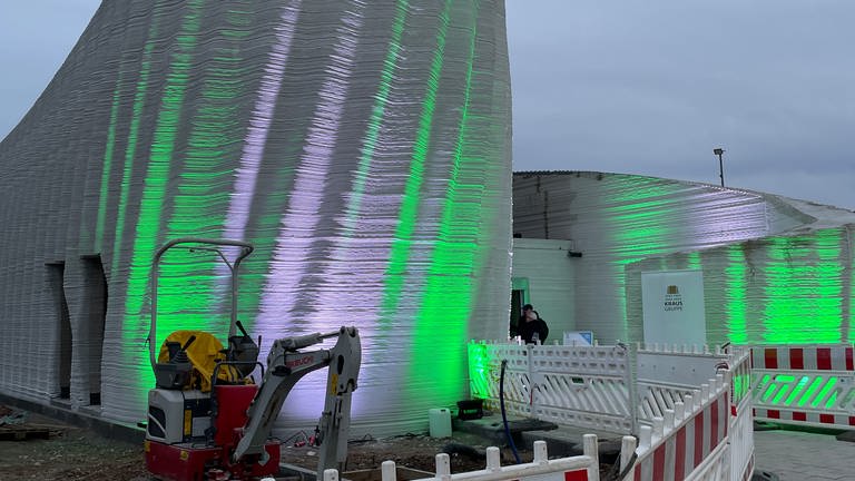 Das gedruckte Gebäude hat eine wellenartige Form. Es wird mit grünen und weißen Strahlern angeleuchtet.
