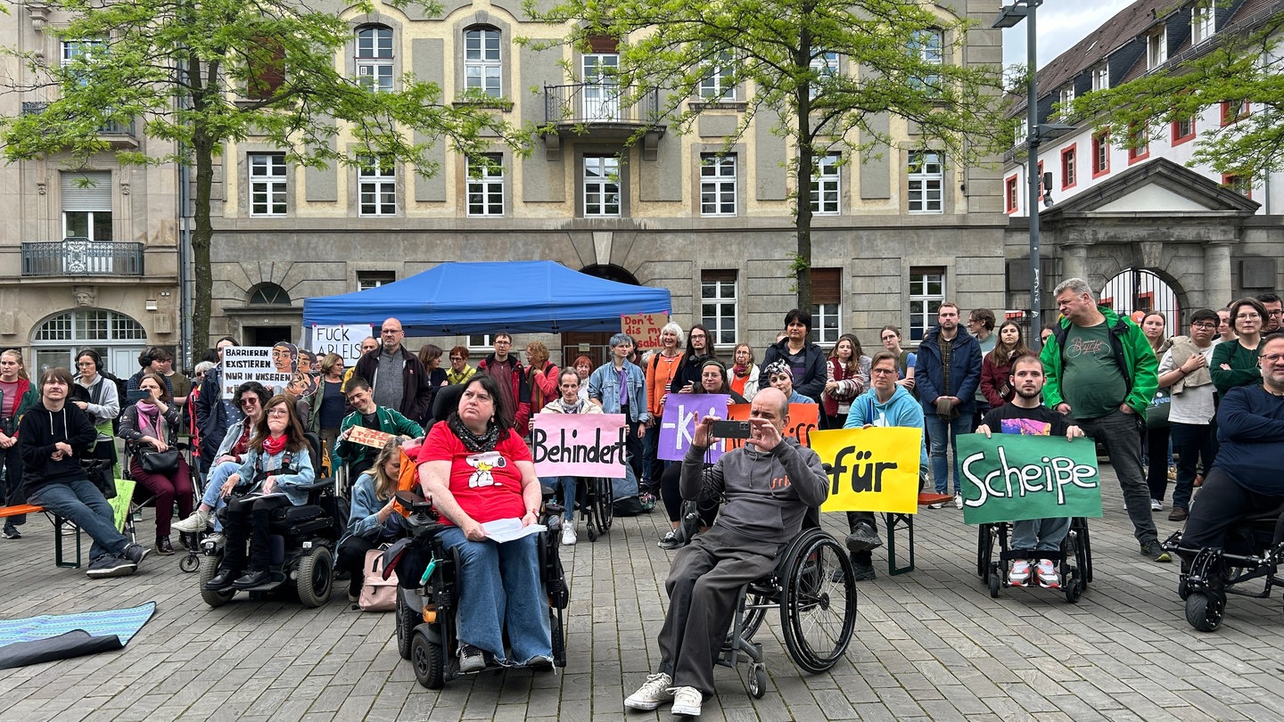 Menschen mit Rollstühlen und ohne haben sich in Heidelberg versammelt. Sie halten Banner und protestieren für mehr Inklusion. (Foto: SWR)