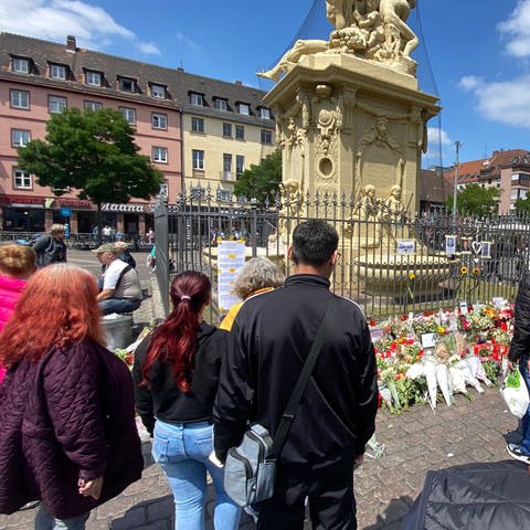Menschen auf dem Marktplatz in Mannheim am Brunnen mit Blumen und Kerzen trauern um toten Polizisten