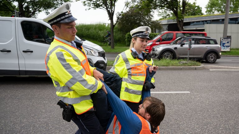 Ein Klimaaktivist der Gruppe "Aufstand der letzten Generation" wird von Polizisten von einer Straße in Stuttgart getragen. (Foto: dpa Bildfunk, picture alliance/dpa | Marijan Murat)