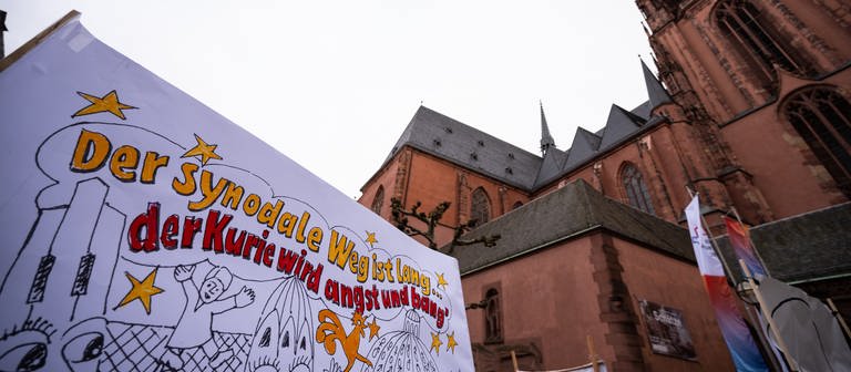 Demonstrantinnen halten vor dem Frankfurter Dom eine Banner mit dem Spruch „Der synodale Weg ist lang … der Kurie wird angst und bang“ hoch. (Foto: dpa Bildfunk, picture alliance/dpa | Andreas Arnold)