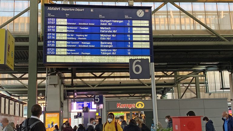 Menschen laufen mit Mund-Nasen-Schutz im Hauptbahnhof Stuttgart unter einer grossen digitalen Anzeige mit Zug-Abfahrtszeiten (Foto: SWR)